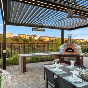 Outdoor kitchen with brick pizza oven under louvered pergola overlooking hillside neighborhood