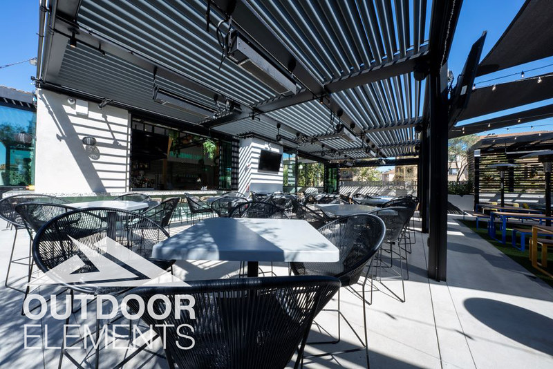 Louvered pergola over outdoor bar patio with wire mesh chairs and string lights