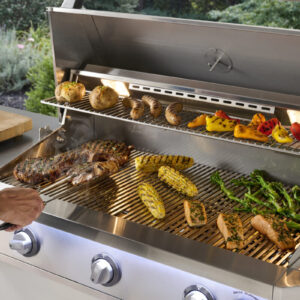 Steak, corn, salmon, and vegetables grilling on open stainless steel gas grill