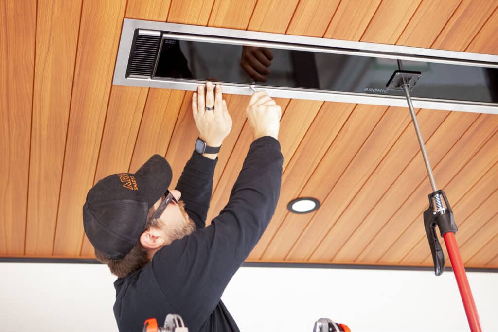 Technician installing overhead infrared patio heater into wooden ceiling