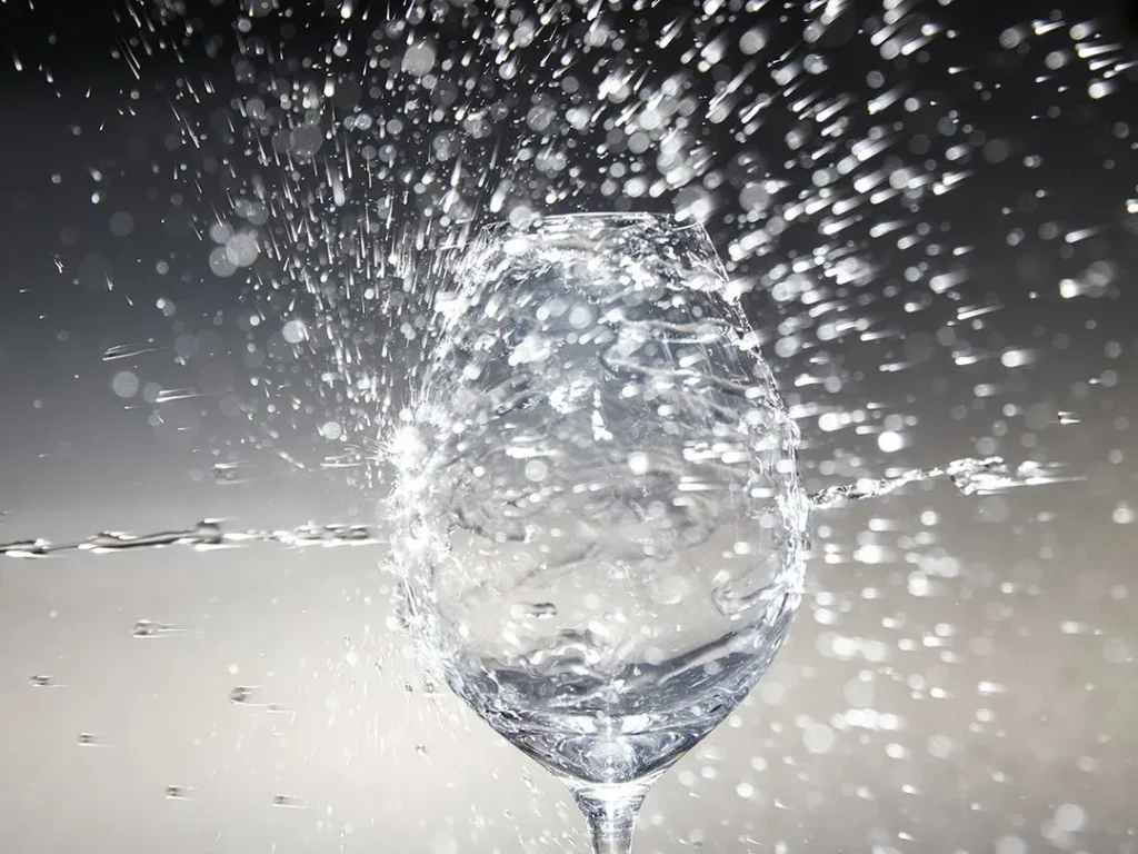 Water splashing dramatically over a wine glass against a dark background