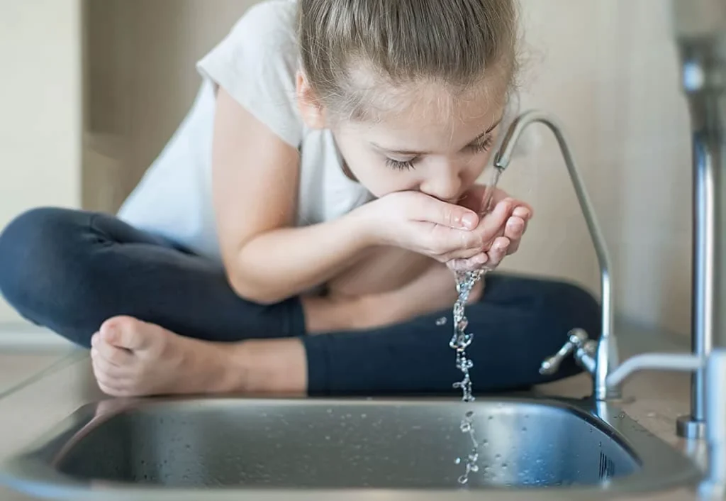Young girl drinking fresh water directly from a kitchen sink faucet