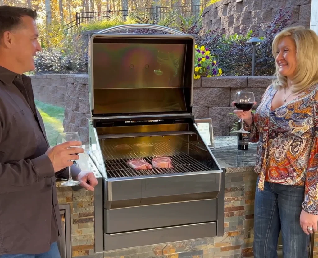 Couple grilling steaks together on an outdoor kitchen grill while enjoying wine