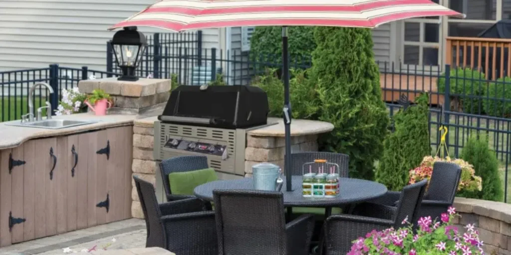 Outdoor patio dining set with striped umbrella beside a built-in stone grill kitchen