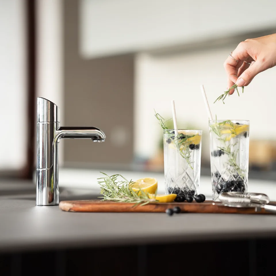 Hand garnishing citrus cocktails at a kitchen sink with modern chrome faucet