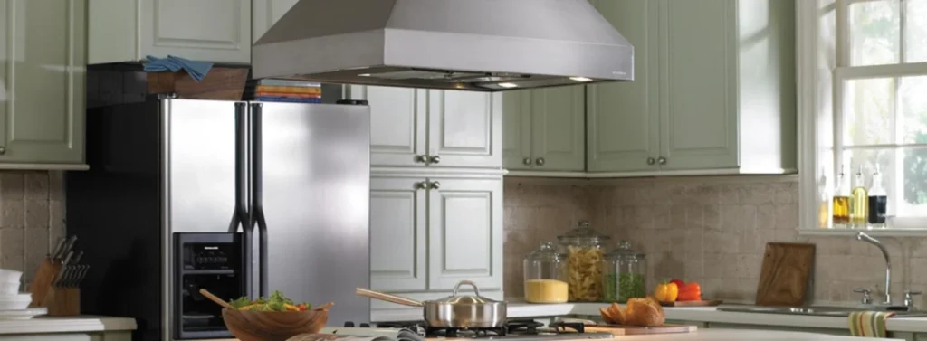 Sage green kitchen with stainless steel range hood, refrigerator and gas cooktop island