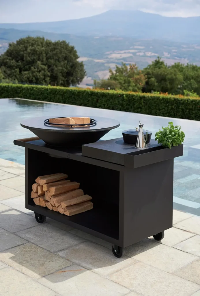 Black wood-burning grill cart with firewood storage beside an infinity pool overlooking hills