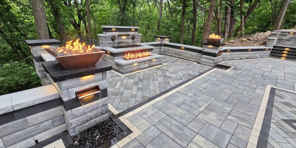 Paver stone patio with matching fire bowls and built-in grill kitchen surrounded by wooded landscaping
