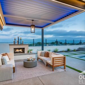 Pergola-covered patio with fireplace and sofa seating overlooking pool at dusk