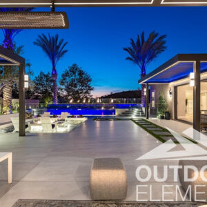 Backyard patio with blue-lit pergolas overlooking infinity-edge pool and palm trees at dusk