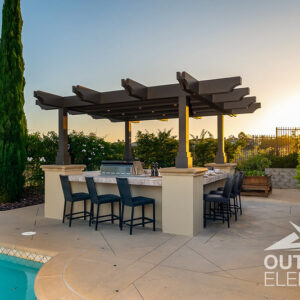 Traditional pergola over tiled outdoor kitchen bar with black stools poolside at sunset