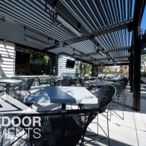 Louvered pergola over outdoor bar patio with wire mesh chairs and string lights