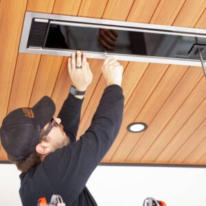 Technician installing overhead infrared patio heater into wooden ceiling